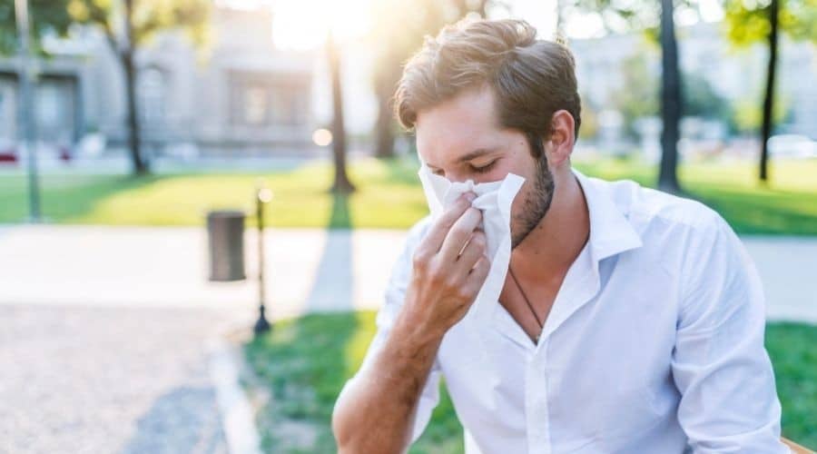 A man sneezing into a tissue. Call C. Woods Company in Tyler, TX for indoor air quality solutions