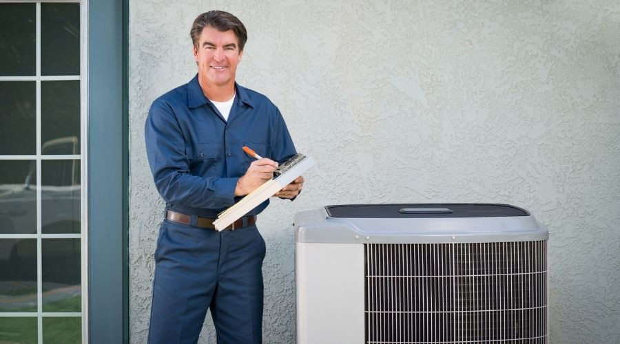 An HVAC tech writing on a clipboard while performing maintenance on an AC unit in Tyler, TX