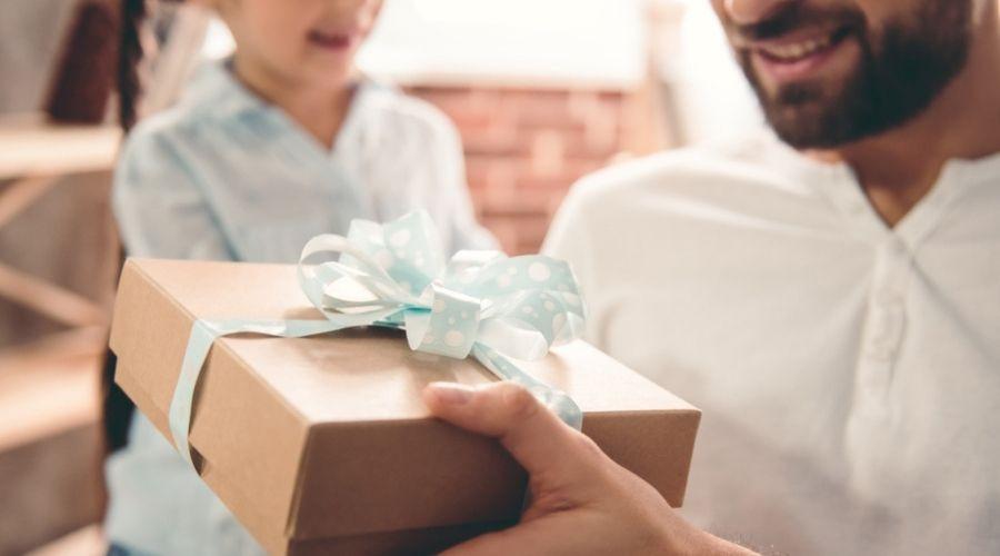 A little girl giving her father a gift box with a blue bow. C. Woods Company for HVAC service in TX
