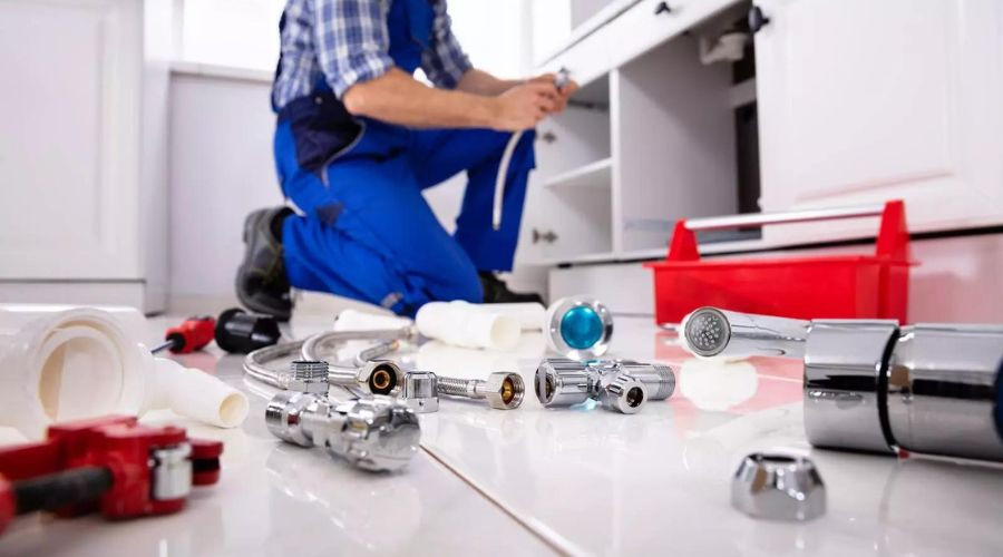A C. Woods company plumber in blue overalls repairing a kitchen sink in Tyler TX