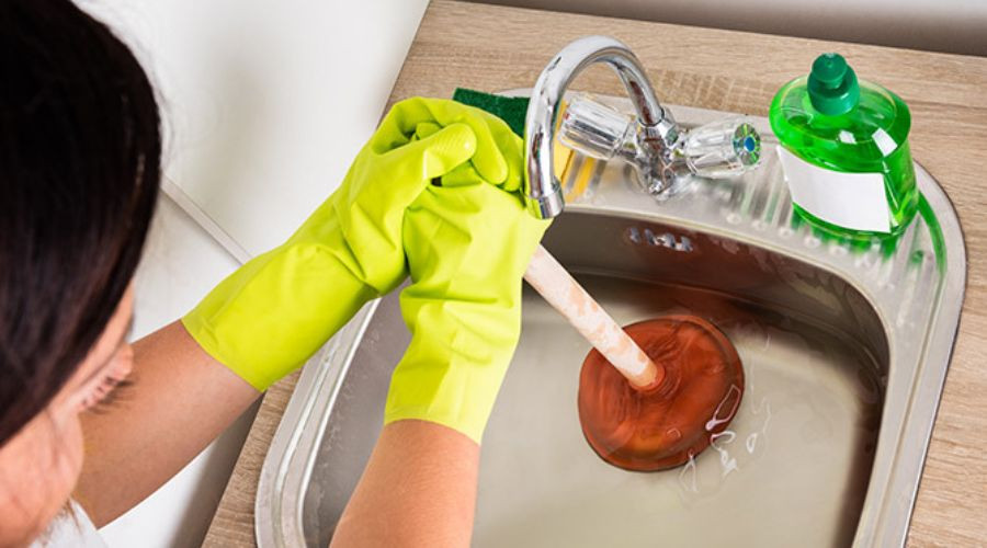 A woman plunging a clogged sink. Call C. Woods Company plumbing team for plumbing needs in Tyler, TX