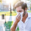 A man sneezing into a tissue. Call C. Woods Company in Tyler, TX for indoor air quality solutions
