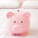 A piggy bank sitting on a white bed. Call C. Woods Company for cost saving solutions