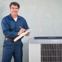 An HVAC tech writing on a clipboard while performing maintenance on an AC unit in Tyler, TX