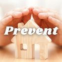 A man holding his hands over a wooden house with the word "Prevent". C. Woods Company in Tyler TX