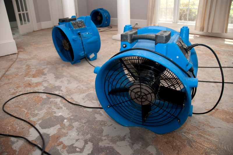 Large blue fans drying flooring from a leak. Call C. Woods Company in Tyler, TX for plumbing repairs