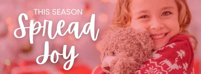 A little girl hold a toy with the words "This Season Spread Joy' from C. Woods Company