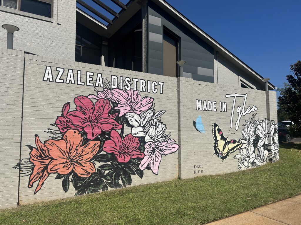 A mural painted on a gray brick wall showing the Azalea District of Tyler, Texas
