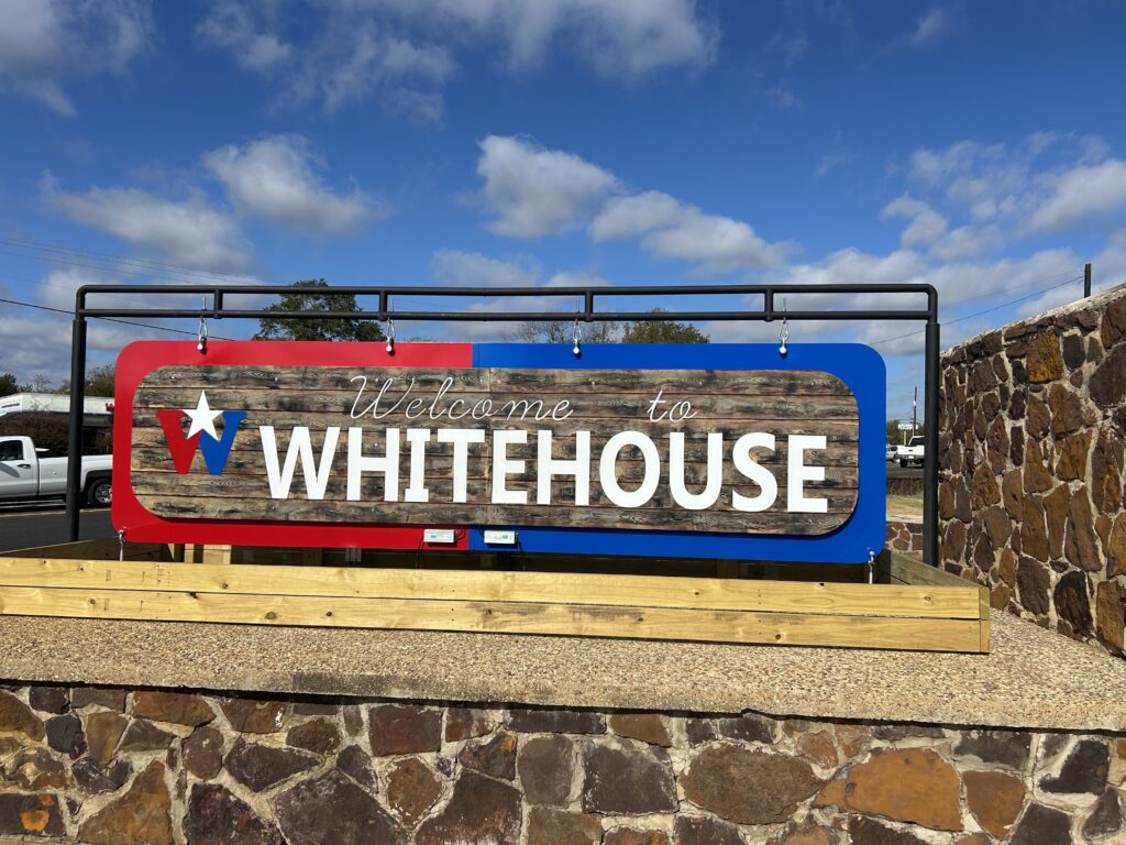 The "Welcome to Whitehouse" Texas sign with white letters on a wooden board.